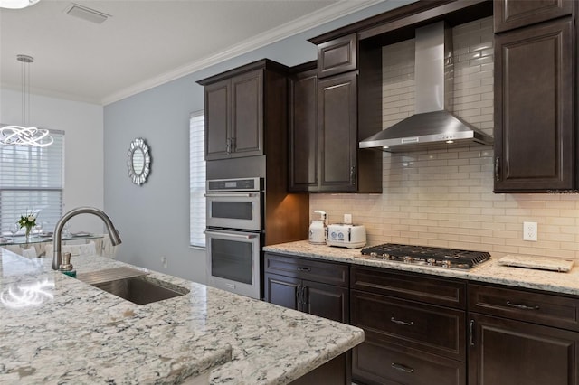 kitchen with sink, stainless steel appliances, ornamental molding, decorative light fixtures, and wall chimney exhaust hood