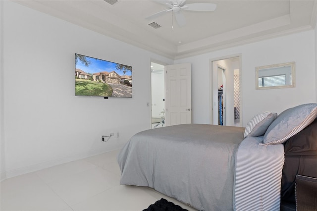 bedroom with ceiling fan, a tray ceiling, light tile patterned floors, and a spacious closet