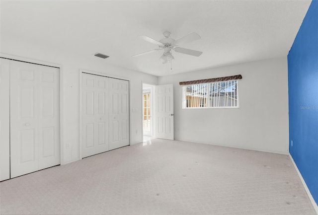 unfurnished bedroom with light carpet, ceiling fan, and multiple closets