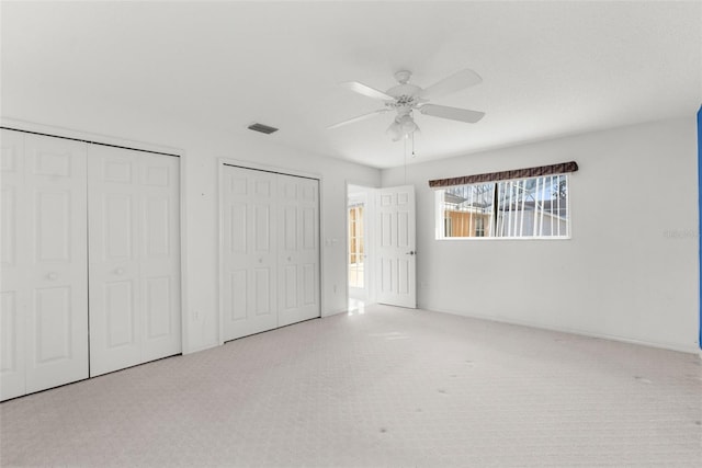 unfurnished bedroom with light carpet, ceiling fan, and multiple closets