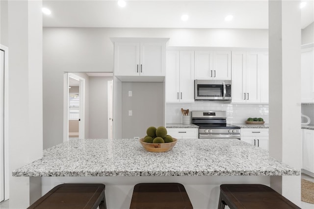 kitchen featuring appliances with stainless steel finishes, tasteful backsplash, white cabinets, a kitchen bar, and light stone countertops