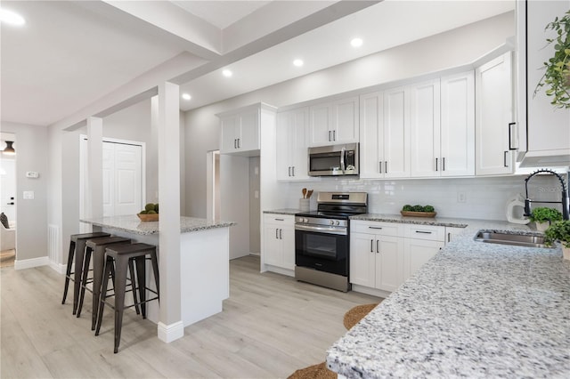 kitchen with appliances with stainless steel finishes, white cabinetry, sink, a kitchen bar, and light stone countertops