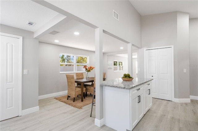 kitchen with white cabinetry, a center island, light stone counters, and light hardwood / wood-style flooring