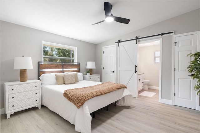 bedroom featuring light hardwood / wood-style flooring, ensuite bath, vaulted ceiling, and a barn door