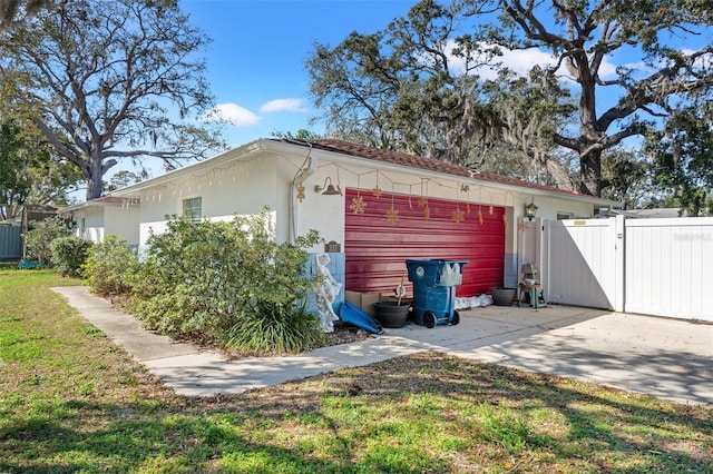 view of side of home with a gate, a yard, fence, and stucco siding