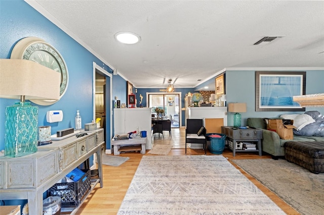 living room featuring crown molding, a textured ceiling, visible vents, and light wood-style floors