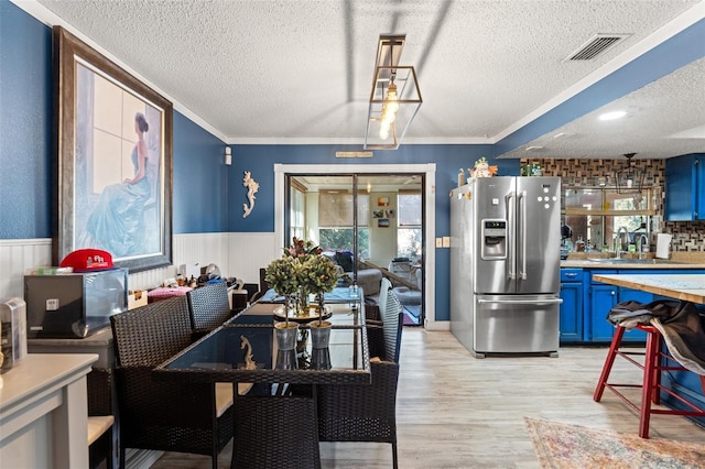 dining space with light wood-style flooring, a wainscoted wall, visible vents, and a textured ceiling