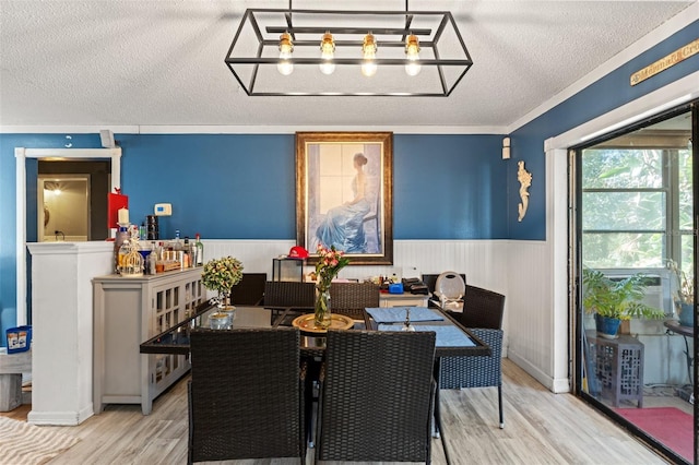 dining space featuring a wainscoted wall, light wood-style flooring, and a textured ceiling