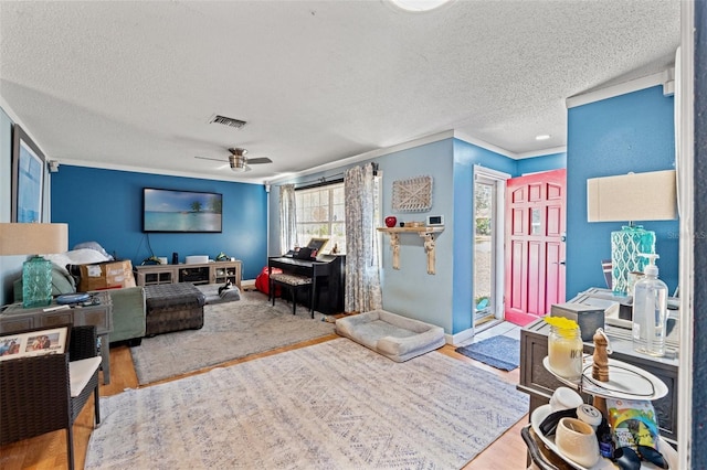 living area with visible vents, a ceiling fan, a textured ceiling, wood finished floors, and baseboards