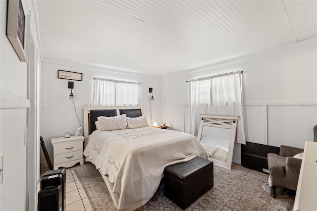 bedroom featuring wainscoting, light tile patterned flooring, and a decorative wall