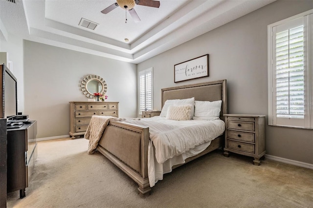 bedroom with a tray ceiling, visible vents, light carpet, and baseboards