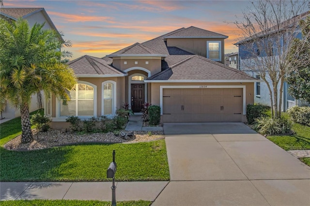 view of front of home with concrete driveway, an attached garage, a lawn, and stucco siding