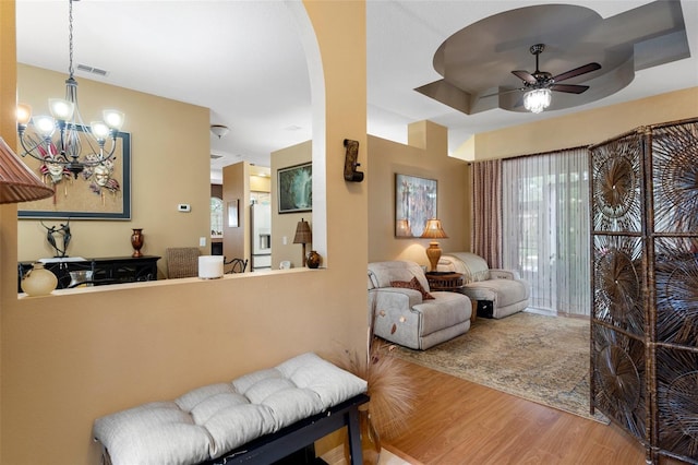 living room with hardwood / wood-style flooring, ceiling fan with notable chandelier, and a tray ceiling