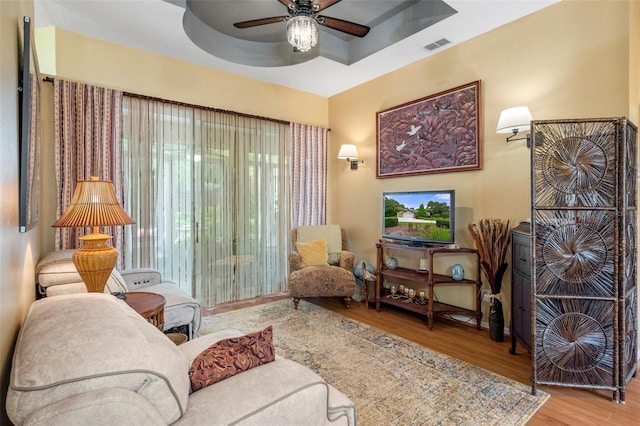 living area with hardwood / wood-style flooring, ceiling fan, and a tray ceiling