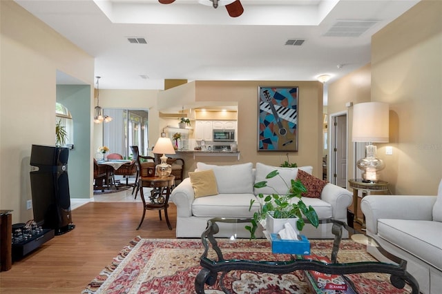 living room featuring ceiling fan with notable chandelier and light hardwood / wood-style flooring