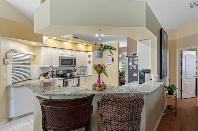 kitchen with stainless steel appliances, light stone countertops, white cabinets, a kitchen bar, and kitchen peninsula