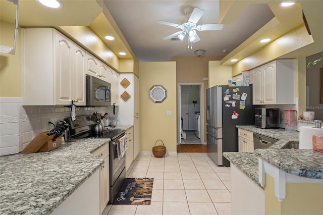 kitchen featuring stainless steel appliances, light stone countertops, light tile patterned floors, and white cabinets