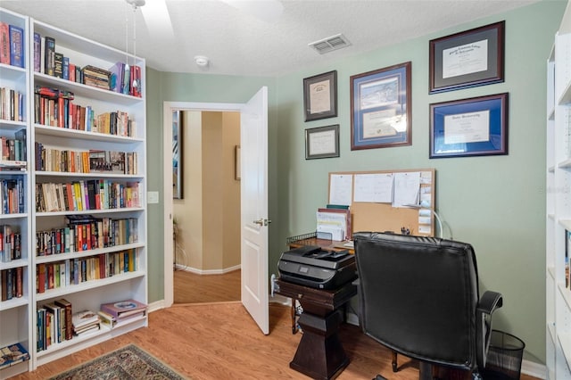 home office with light hardwood / wood-style floors and a textured ceiling