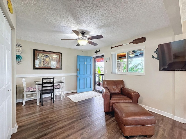 living area with dark wood-type flooring, ceiling fan, and a textured ceiling