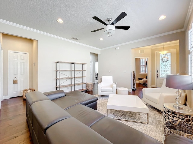 living room featuring a textured ceiling, ornamental molding, wood finished floors, and visible vents