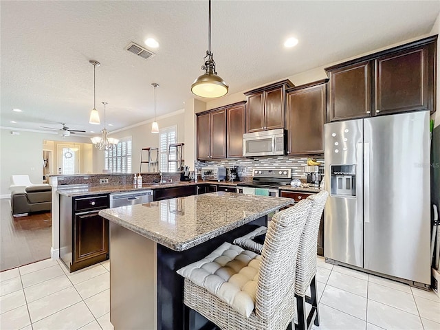 kitchen featuring light tile patterned floors, a peninsula, a kitchen breakfast bar, hanging light fixtures, and appliances with stainless steel finishes