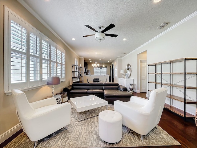 living room featuring dark wood finished floors, visible vents, ornamental molding, a textured ceiling, and ceiling fan with notable chandelier