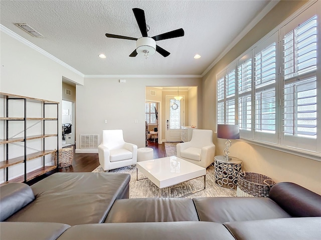 living room featuring a textured ceiling, ornamental molding, wood finished floors, and visible vents