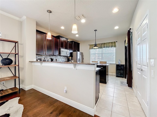 kitchen featuring stainless steel appliances, visible vents, hanging light fixtures, a peninsula, and a kitchen bar