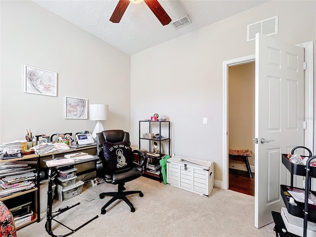 office area with a textured ceiling, ceiling fan, visible vents, and light colored carpet