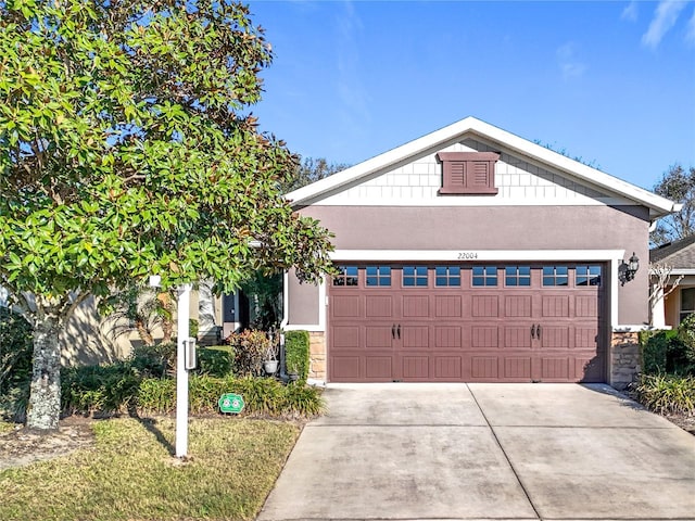 view of front of property with stone siding, an attached garage, driveway, and stucco siding