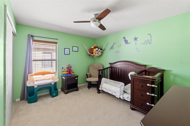 bedroom with light carpet, a textured ceiling, a crib, and ceiling fan