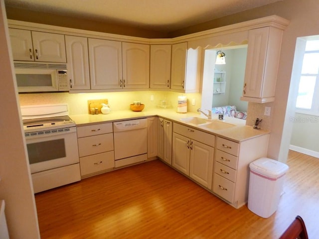 kitchen with light countertops, white appliances, a sink, and light wood-style floors