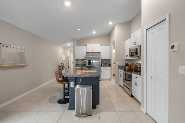 kitchen featuring a breakfast bar, a center island with sink, light tile patterned floors, appliances with stainless steel finishes, and white cabinets