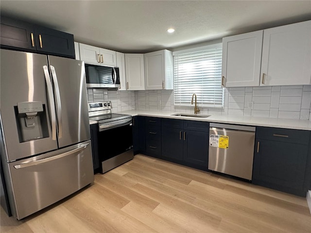 kitchen featuring sink, light wood-type flooring, appliances with stainless steel finishes, decorative backsplash, and white cabinets