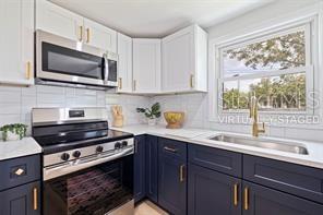 kitchen featuring sink, blue cabinetry, appliances with stainless steel finishes, white cabinetry, and decorative backsplash