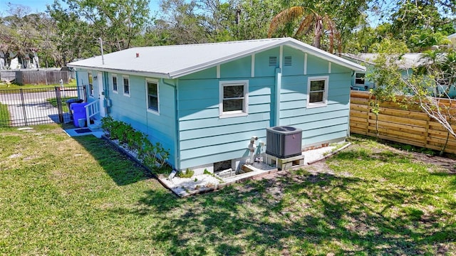 rear view of house featuring central air condition unit, a lawn, and fence