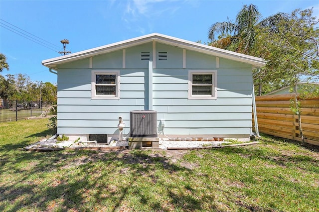 rear view of house featuring a yard, central AC unit, and fence