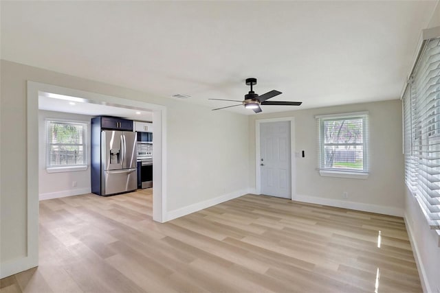spare room with light wood-type flooring, visible vents, a ceiling fan, and baseboards