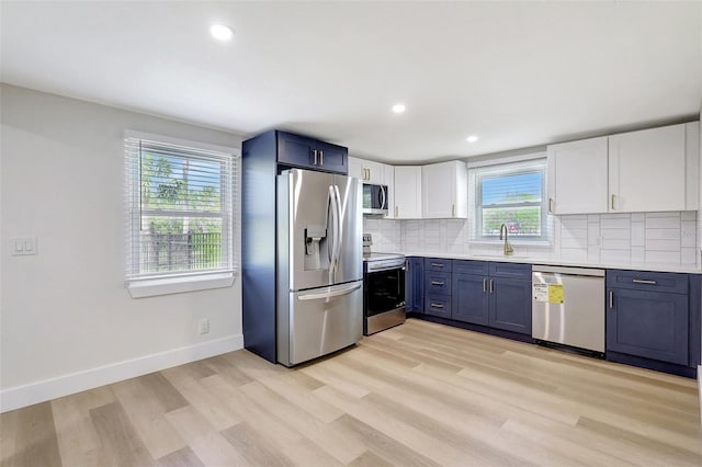 kitchen with a sink, light wood finished floors, light countertops, backsplash, and appliances with stainless steel finishes