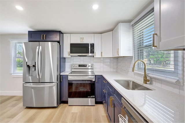 kitchen featuring stainless steel appliances, a sink, white cabinetry, light wood-style floors, and blue cabinetry