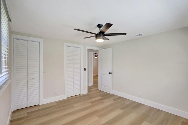 unfurnished bedroom featuring baseboards, visible vents, multiple closets, and light wood finished floors