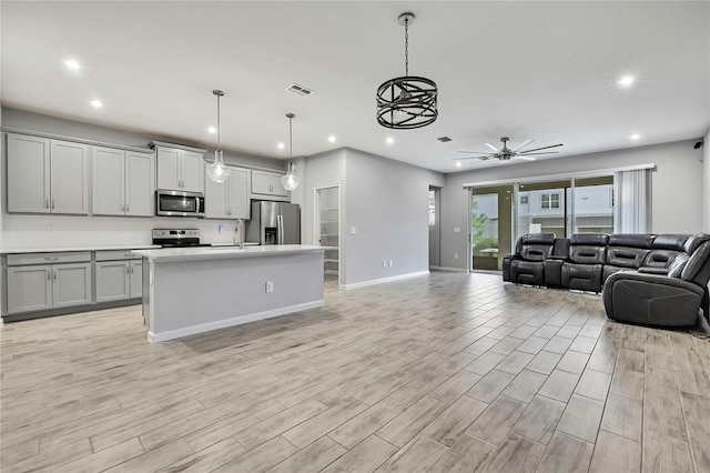 kitchen with a center island with sink, gray cabinets, pendant lighting, stainless steel appliances, and light hardwood / wood-style floors