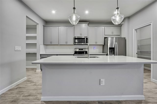 kitchen with hanging light fixtures, a center island with sink, gray cabinets, and appliances with stainless steel finishes