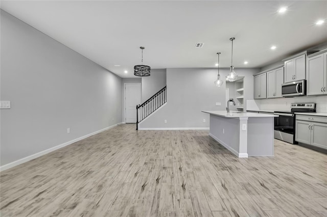 kitchen with appliances with stainless steel finishes, decorative light fixtures, gray cabinets, and a center island with sink