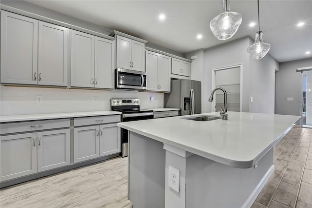 kitchen with an island with sink, appliances with stainless steel finishes, sink, and decorative light fixtures