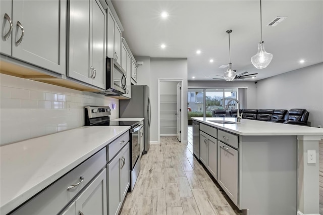 kitchen featuring sink, gray cabinetry, tasteful backsplash, a center island with sink, and appliances with stainless steel finishes