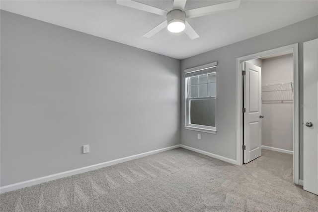 unfurnished bedroom featuring light carpet, a walk in closet, a closet, and ceiling fan