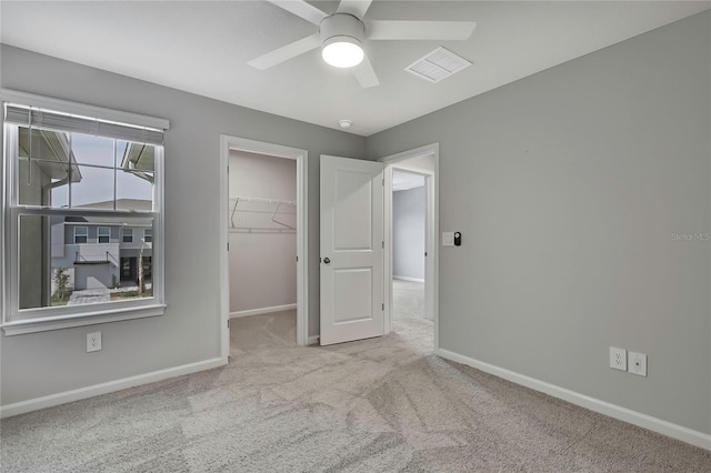 unfurnished bedroom with a walk in closet, light colored carpet, a closet, and ceiling fan