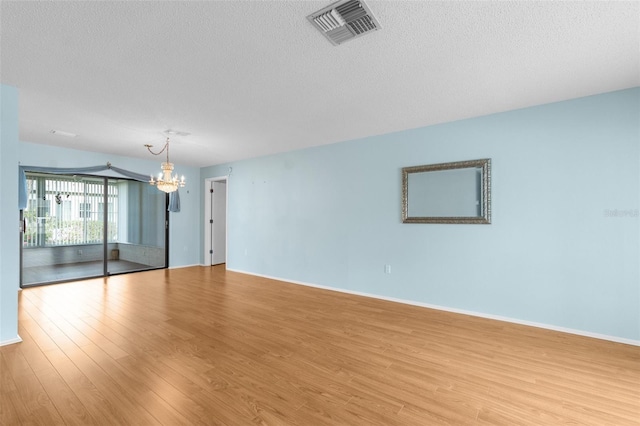 unfurnished room featuring a textured ceiling, light hardwood / wood-style floors, and a chandelier