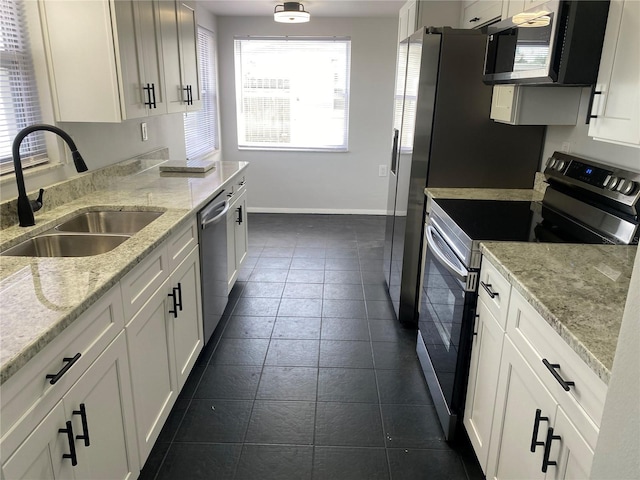 kitchen with sink, white cabinetry, light stone counters, appliances with stainless steel finishes, and dark tile patterned floors